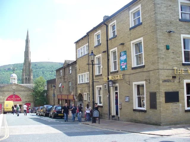 A historic brick building named "The Westgate" sits on a street with cars parked alongside, and a tall church spire rises in the distance.